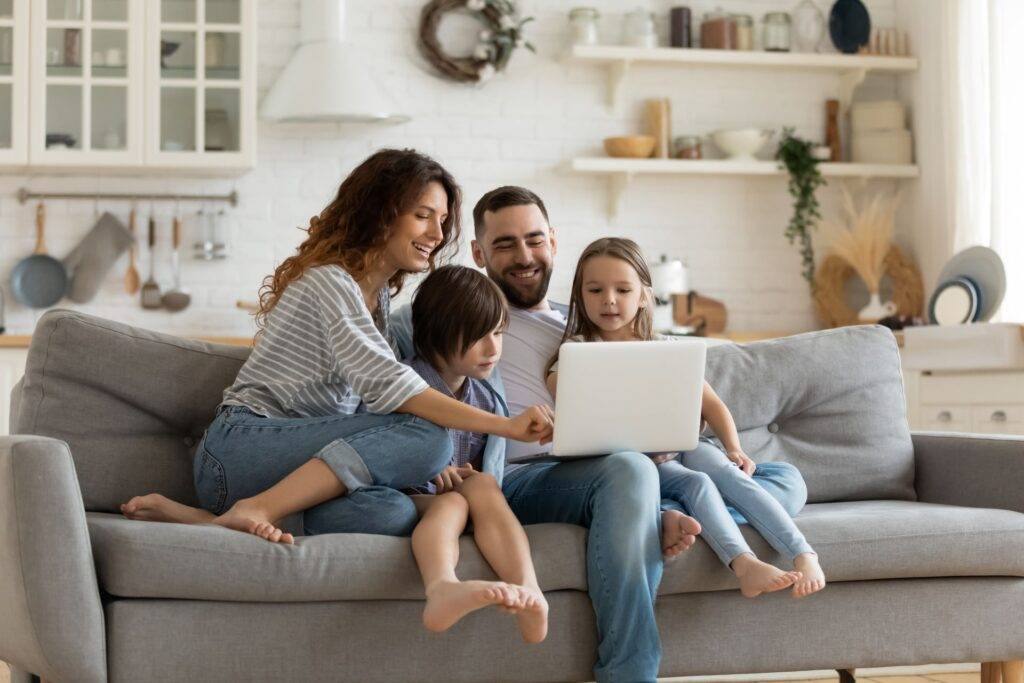 Eine glückliche Familie sitzt auf dem Sofa und schaut gemeinsam auf einen Laptop, während sie digitale Fotos und Erinnerungen genießen, die sie durch das Scannen und Digitalisieren von alten Bildern erstellt haben.