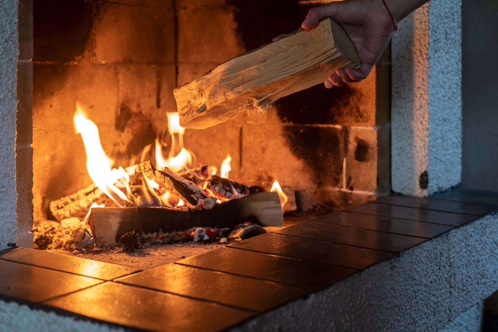 Hand legt Holzscheit in Kamin mit knisterndem Feuer.