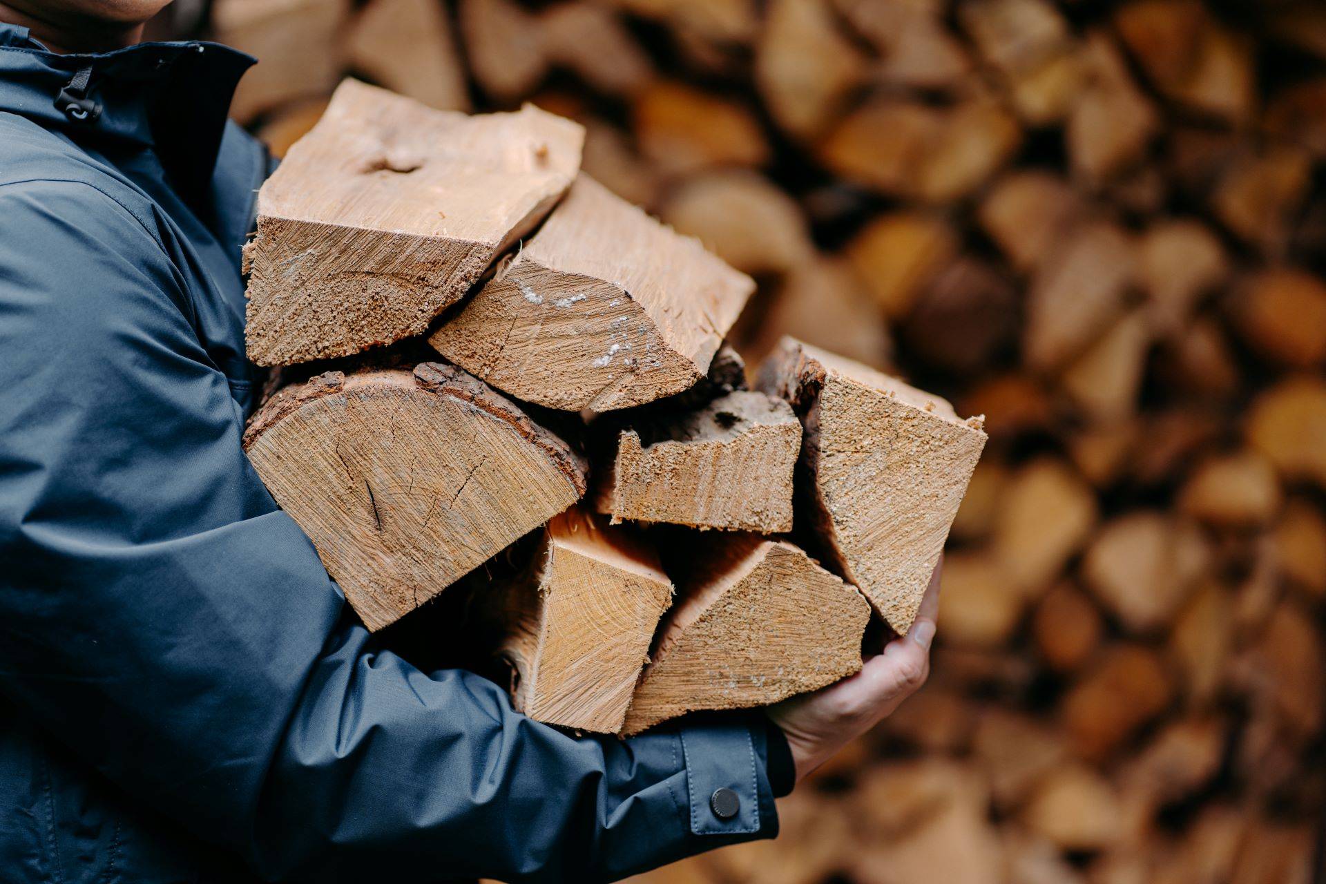 Person trägt Holzscheite vor Brennholzstapel, nachhaltige Holzlagerung.