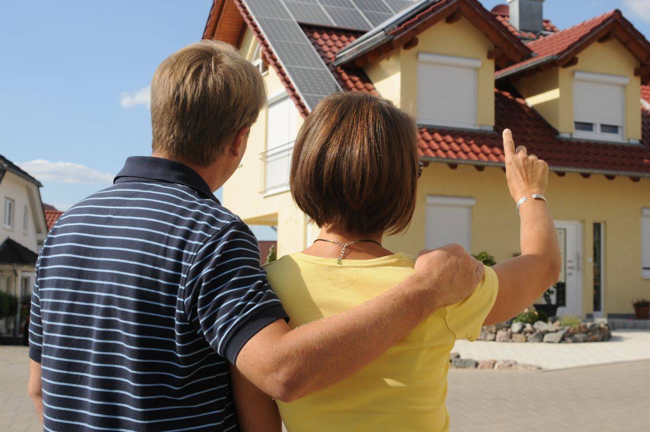 paar steht vor einem modernen einfamilienhaus und zeigt darauf immobilienmakler rosenheim unterstuetzt bei der auswahl